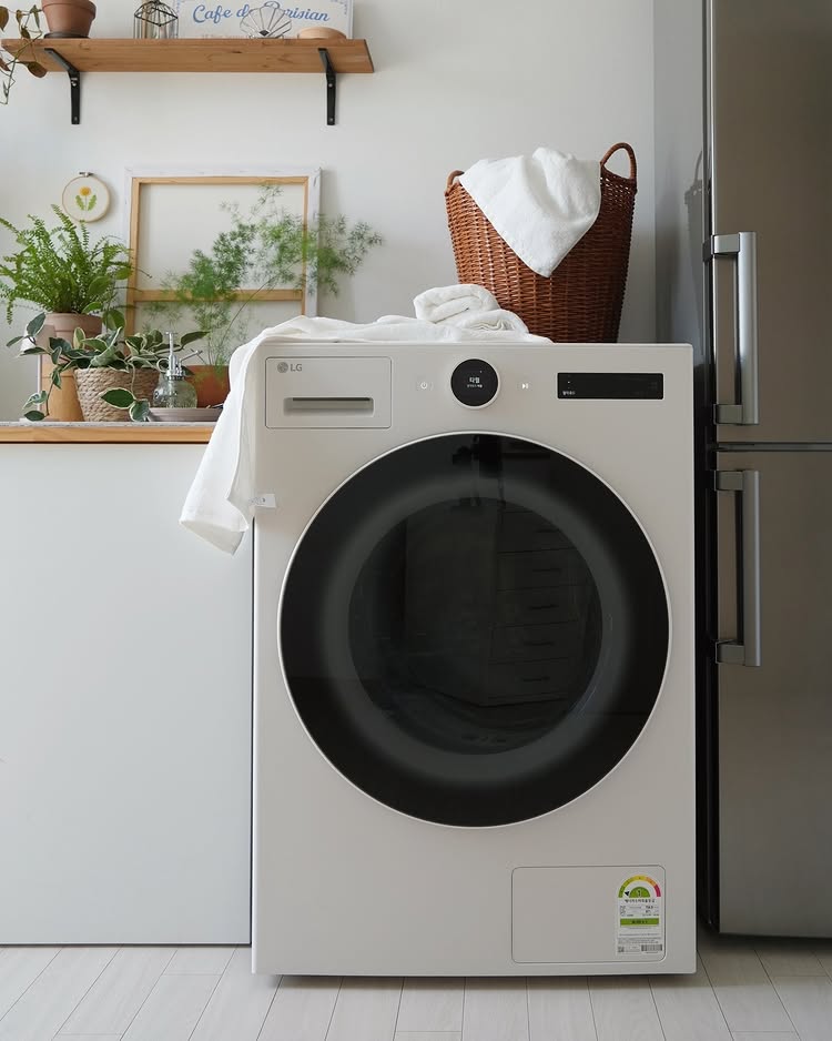 LG 트롬 오브제컬렉션 건조기가 주방 인테리어와 조화를 이루며 배치된 모습. 건조기 위에는 수건과 빨래 바구니가 놓여 있음.