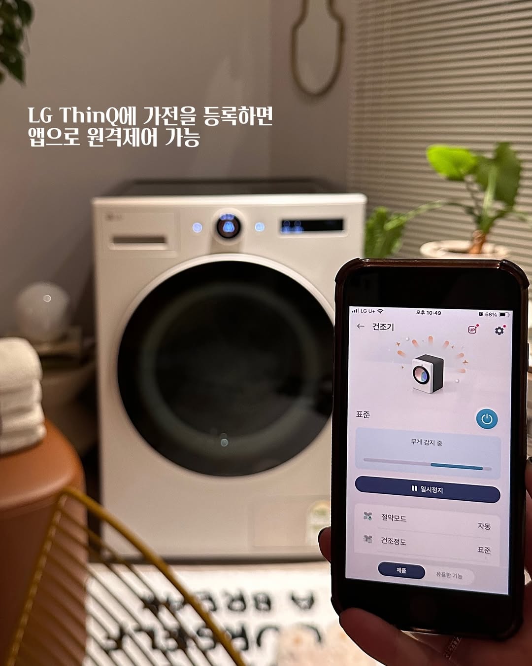 LG 트롬 오브제컬렉션 건조기가 LG ThinQ 앱을 통해 원격 제어되는 모습. 스마트폰 화면에는 건조 진행 상태와 옵션 설정이 표시되어 있음.