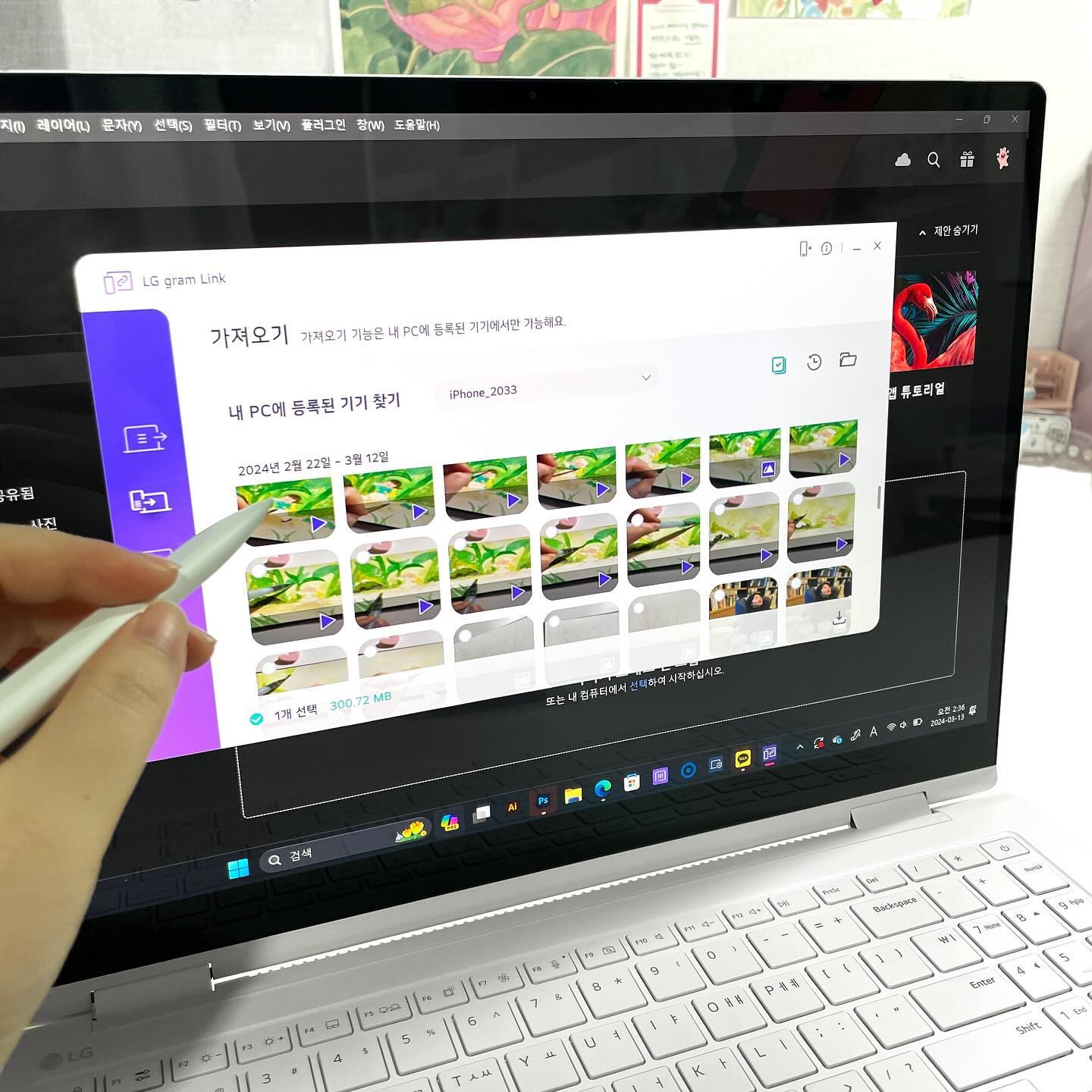 사용자가 펜을 사용해 노트북 화면에서 LG gram Link를 통해 스마트폰과 파일을 전송하는 모습. 여러 개의 영상 파일이 표시되어 있으며, 하나의 파일이 선택된 상태임.