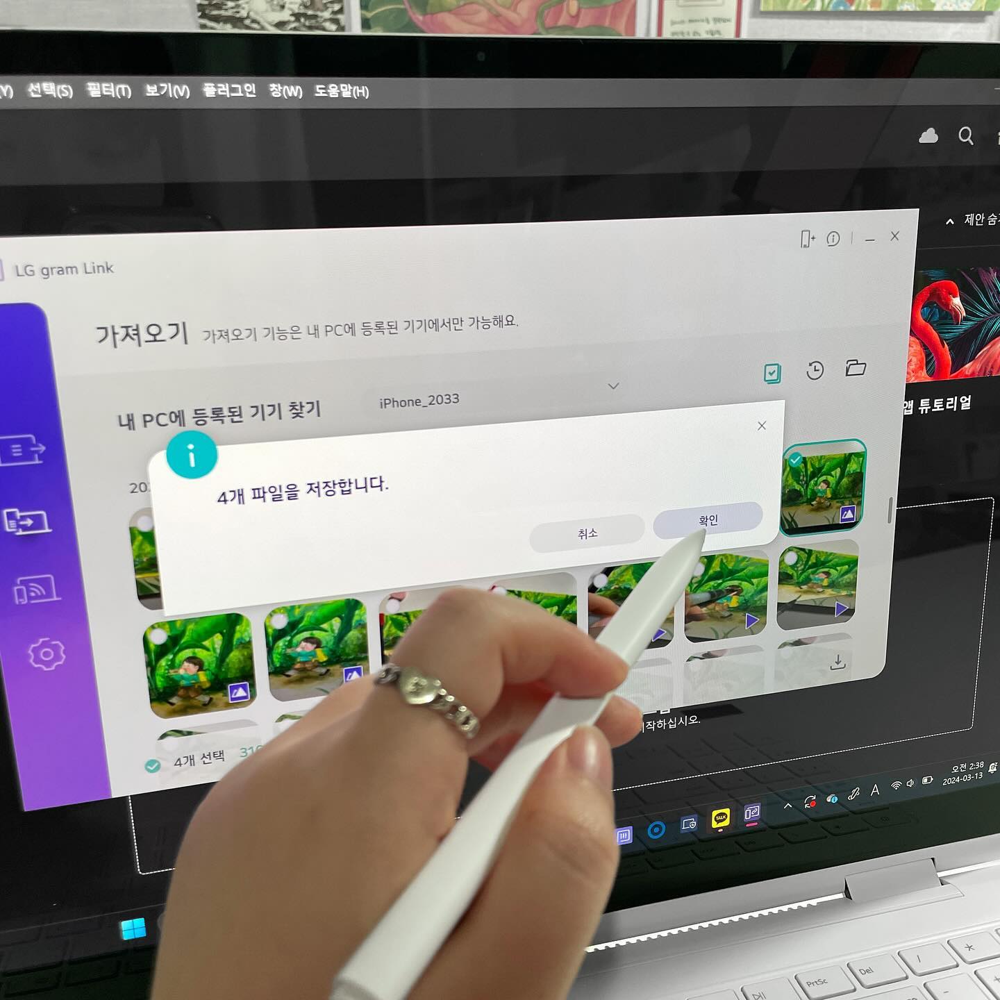 사용자가 								펜을 사용하여 노트북 화면에서 LG gram Link를 통해 스마트폰과 파일을 전송하는 모습. 4개 파일을 저장합니다. 라는 팝업 창이 표시되어 있으며, 확인 버튼을 누르려는 손이 보임.