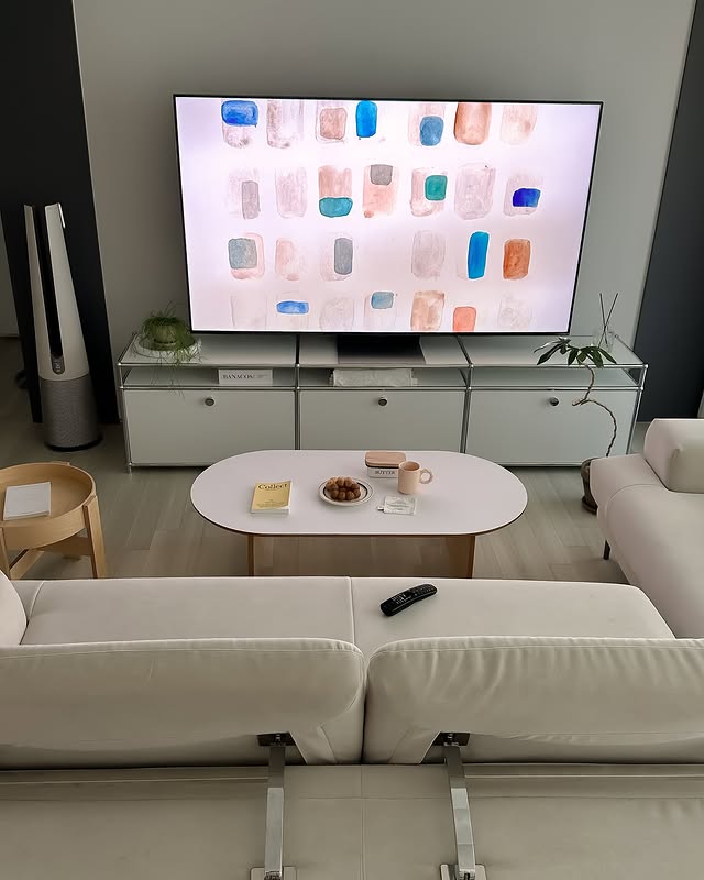 LG QNED evo TV가 넓은 거실 중앙에 설치되어 있으며, 모던한 인테리어 속에서 TV 화면에 추상적인 패턴이 표시되어 있다. 소파와 테이블이 조화롭게 배치된 공간이 보인다.