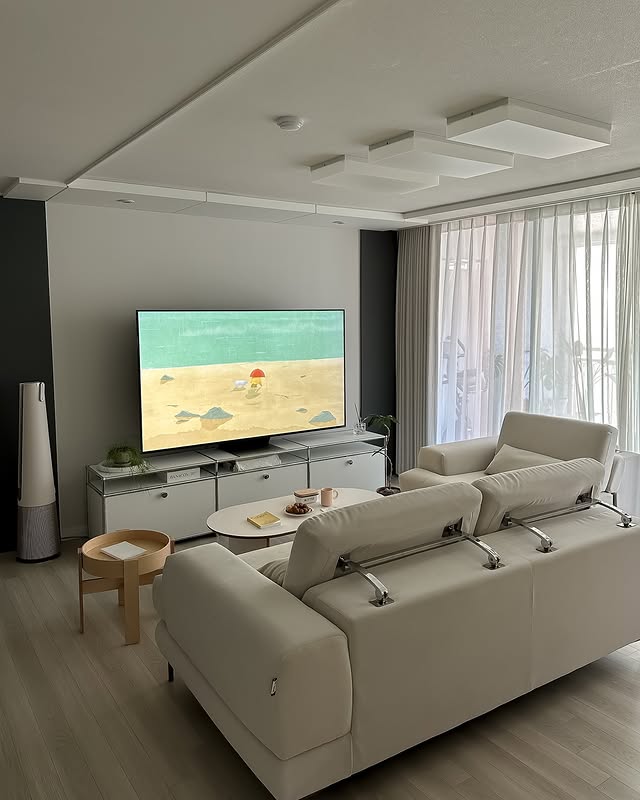 LG QNED evo TV가 화이트 톤의 거실에 설치되어 있으며, 소파와 함께 넓고 깔끔한 인테리어가 돋보인다. TV 화면에는 애니메이션 배경으로 보이는 해변 장면이 표시되어 있다.