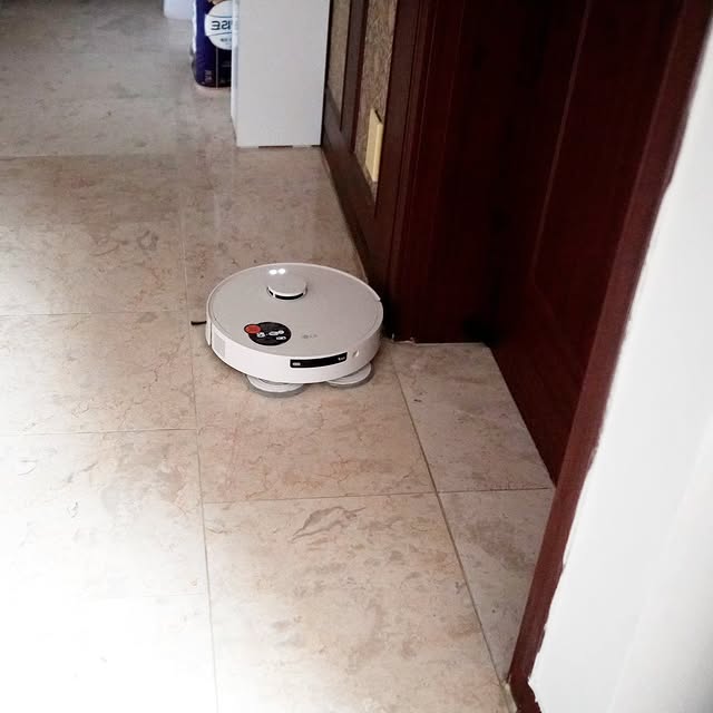 LG 코드제로 로보킹 AI 올인원이 현관 바닥을 청소하는 모습. 로봇청소기가 자동으로 구석구석을 청소하며 바닥의 먼지를 제거함.