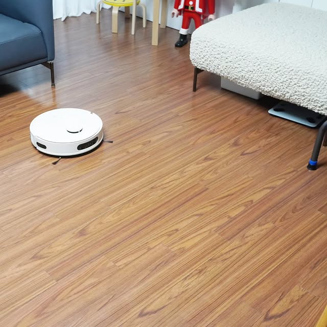 거실 바닥을 청소하는 LG 코드제로 로보킹 AI 올인원. 주변에 소파와 침대가 놓여 있으며, 나무 바닥 위를 청소하는 모습.