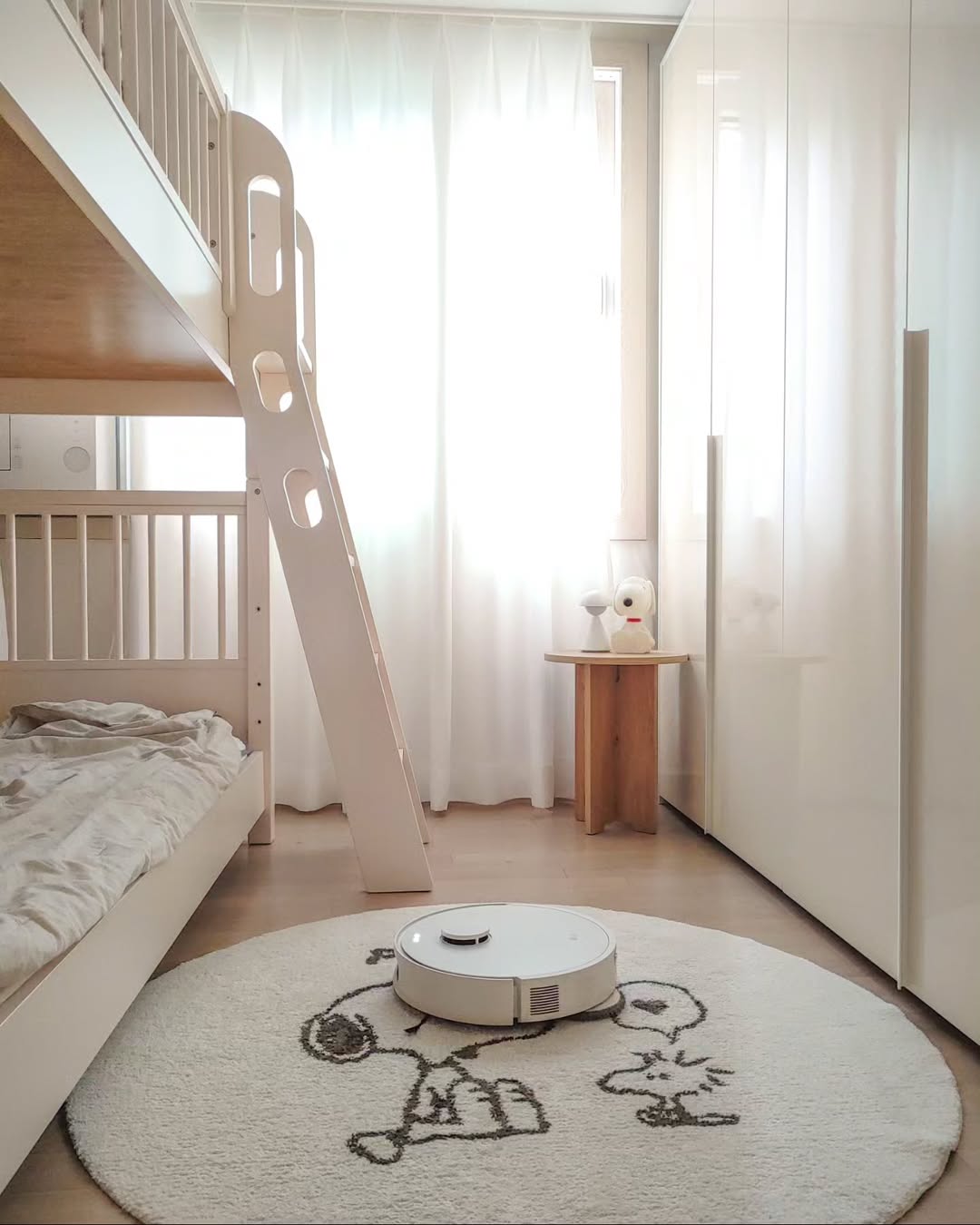 LG 코드제로 로보킹 AI 올인원이 아이 방에서 둥근 러그 위를 청소하는 모습. 이층 침대, 화이트 옷장, 스누피 디자인의 러그가 따뜻한 분위기를 연출하며, 로봇청소기가 아이 방도 깨끗하게 관리할 수 있음을 보여준다.
