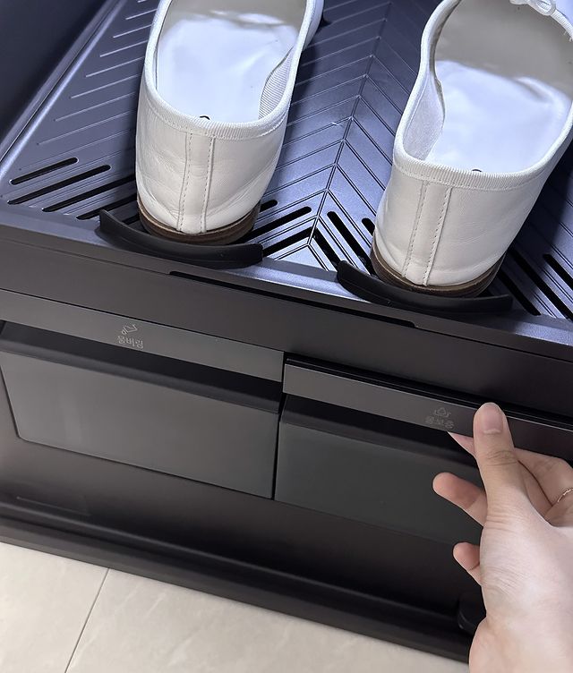스타일러 오브제컬렉션 슈케어 내부에 슬리퍼가 놓여 있고, 하단 수납칸을 손으로 열고 있는 모습.