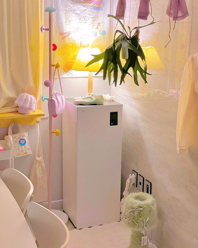 스타일러 오브제컬렉션 슈케어가 방 한쪽에 배치되어 있으며, 상단에 작은 조명과 식물이 놓여 있고, 주변에는 파스텔톤 소품들이 조화를 이룸.