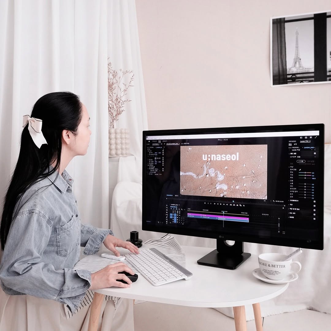 LG 스마트모니터를 사용해 영상 편집 프로그램을 실행한 모습이다. 여성이 키보드와 마우스를 활용해 작업을 진행하고 있으며, 책상 위에는 커피잔과 다양한 작업 도구들이 놓여 있다.