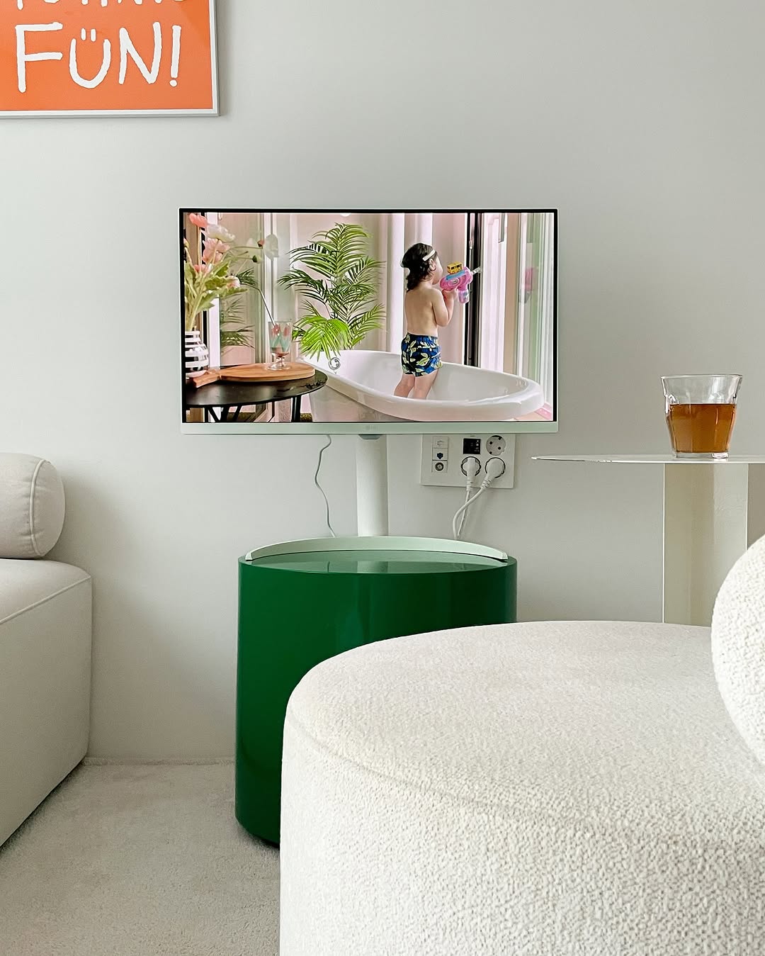 LG 스마트 모니터가 녹색 원형 테이블 위에 설치되어 있으며, 화면에는 목욕하는 아이의 영상이 재생되고 있다. 주변에는 거실 소품과 음료가 놓여 있어 따뜻한 분위기를 연출한다.