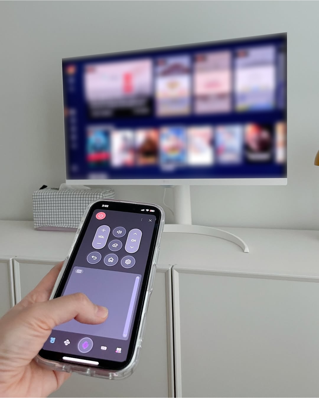 LG 스마트 모니터 앞에서 스마트폰을 활용해 화면을 조작하는 모습. 스마트폰 화면에는 ThinQ 앱의 리모컨 버튼이 노출되고 있으며, 사용자가 조작 중이다.