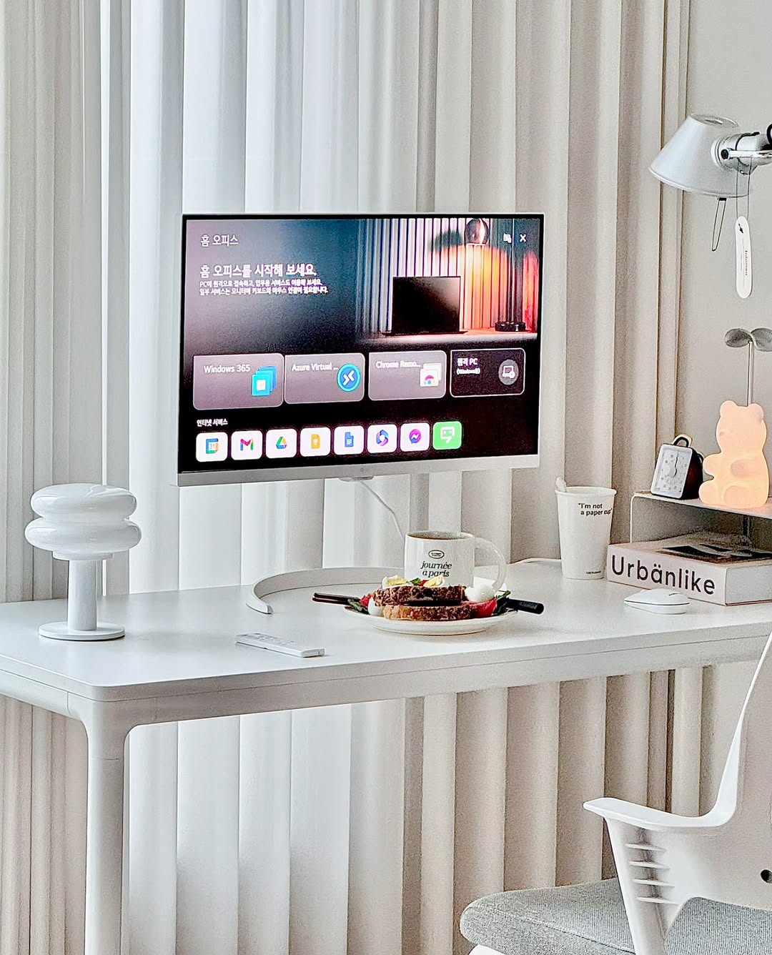 책상 위에 놓인 LG 스마트 모니터로 홈 오피스 환경을 구성한 모습. 모니터 화면에는 원격 PC 접속 및 다양한 업무용 앱이 실행되고 있으며, 책상 위에는 커피와 간식이 놓여 있다.