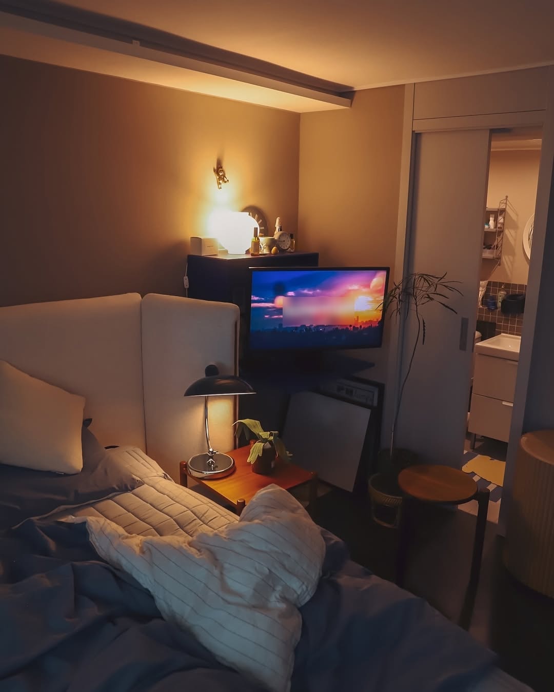 침대에서 바라본 LG 스마트 모니터 화면. 어두운 공간 속에서 따뜻한 조명이 켜져 있으며, 모니터에는 석양이 지는 장면이 재생되고 있다.