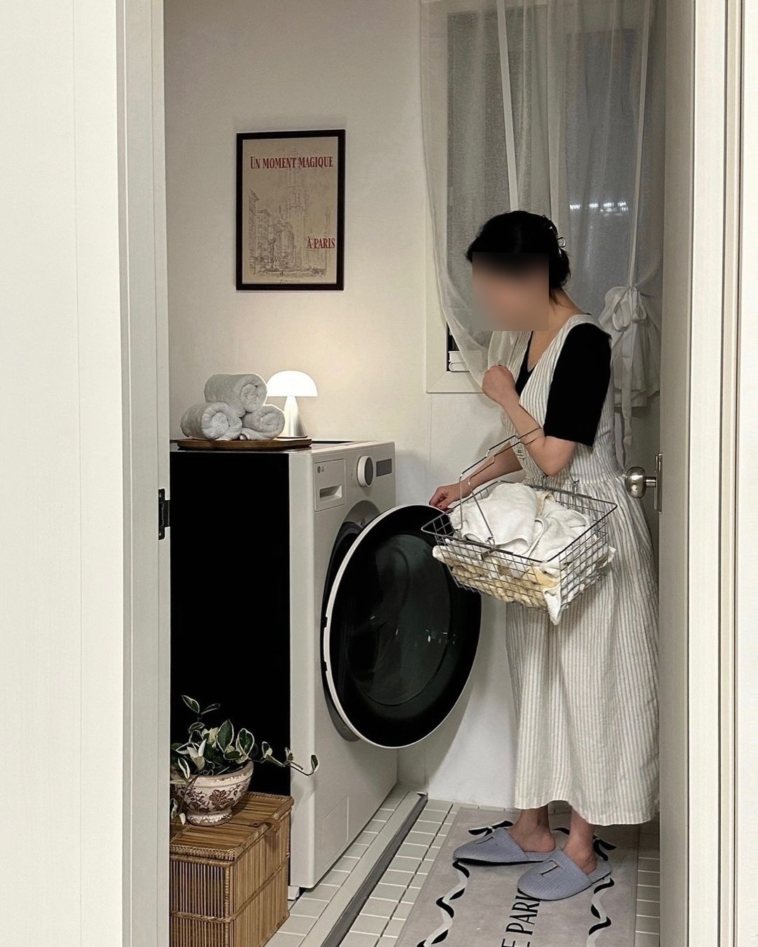 문이 열린 세탁실에 워시콤보 앞에서 바구니에 세탁물을 담고 있는 여성이 문을 열고 있는 다른 각도 모습.