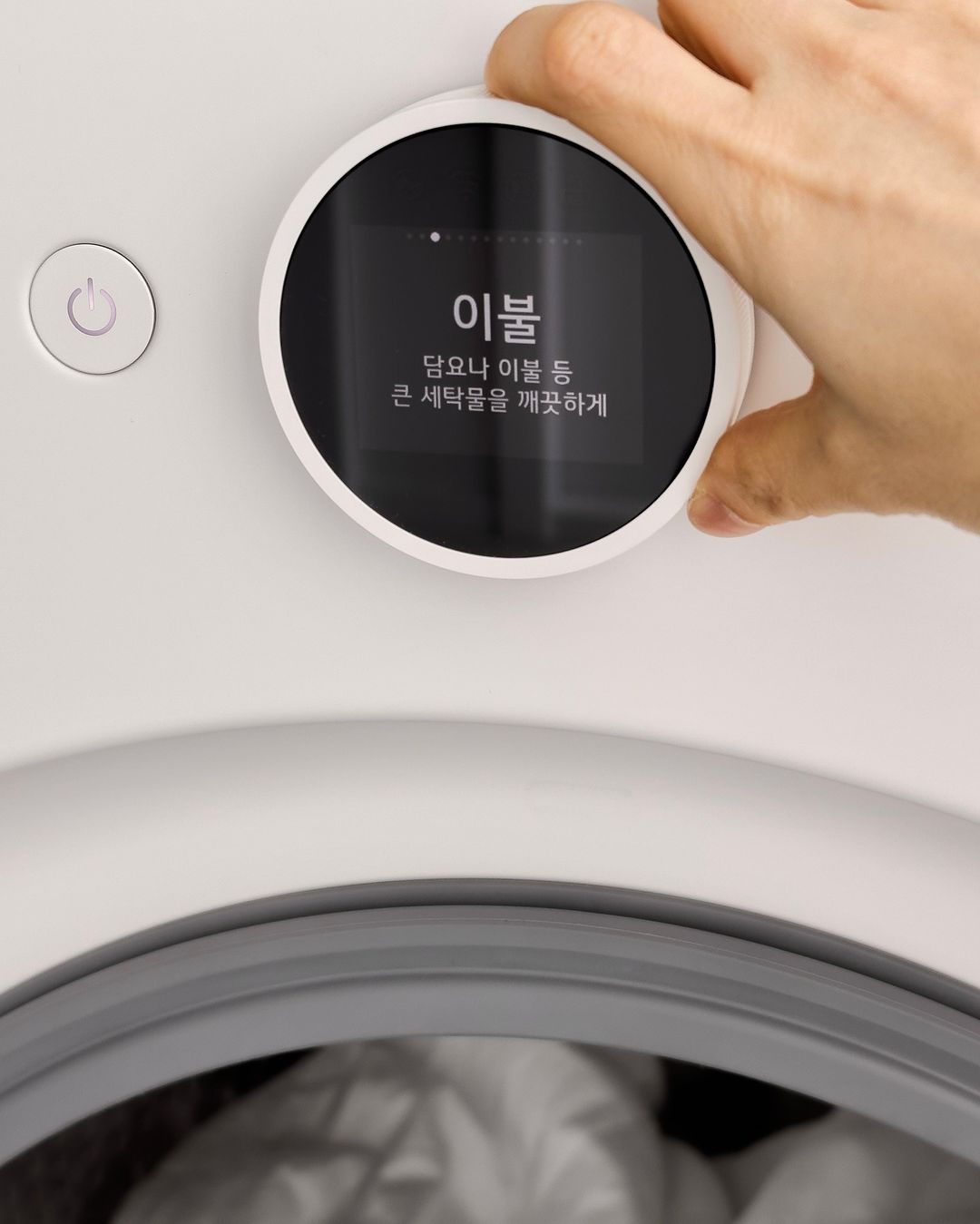 워시콤보의 다이얼을 조작하는 손, 화면에 옵션(이불, 담요나 이불 등 큰 세탁물을 깨끗하게)이 표시되어 있음, 바로 옆에 직관적인 전원 버튼이 있음.