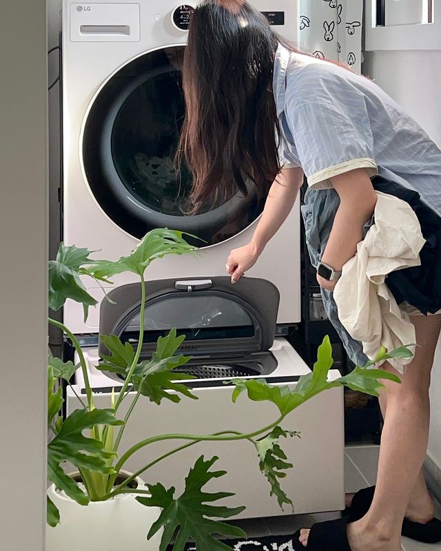 워시콤보 미니워시에 세탁물을 넣고 있는 여성. 앞에는 큰 화분이 놓여 있음.