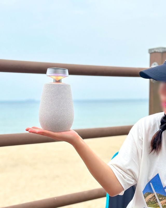 푸른 바다와 하늘이 뒤로 보이는 바닷가에서 손바닥 위에 올려진 엑스붐 360.