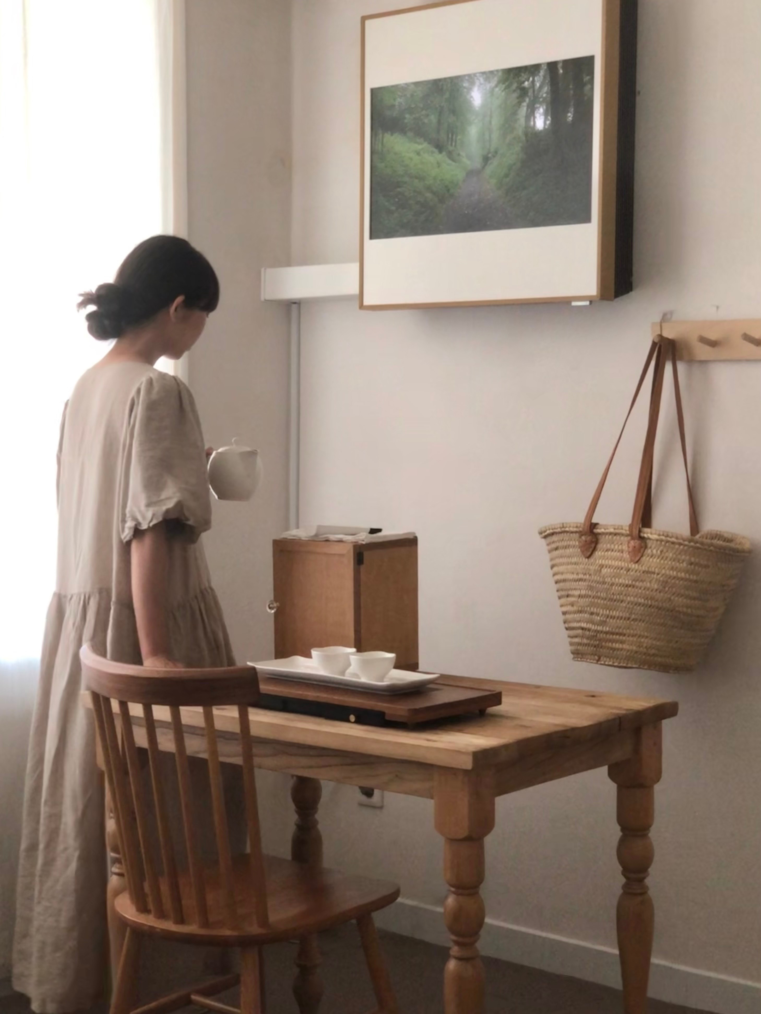 LG 휘센 오브제컬렉션 아트쿨 에어컨이 벽에 설치된 모습으로, 화면에는 초록색 숲길 이미지가 표시되어 있음. 여성 사용자가 주전자와 찻잔을 들고 서 있는 모습.