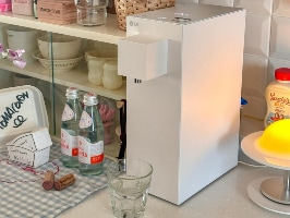 주방 조리대 위에 LG 정수기가 놓여 있으며, 앞에는 유리컵이 있고 주변에는 물병, 소스 병, 그릇 등이 정리된 선반과 조명이 배치되어 있음