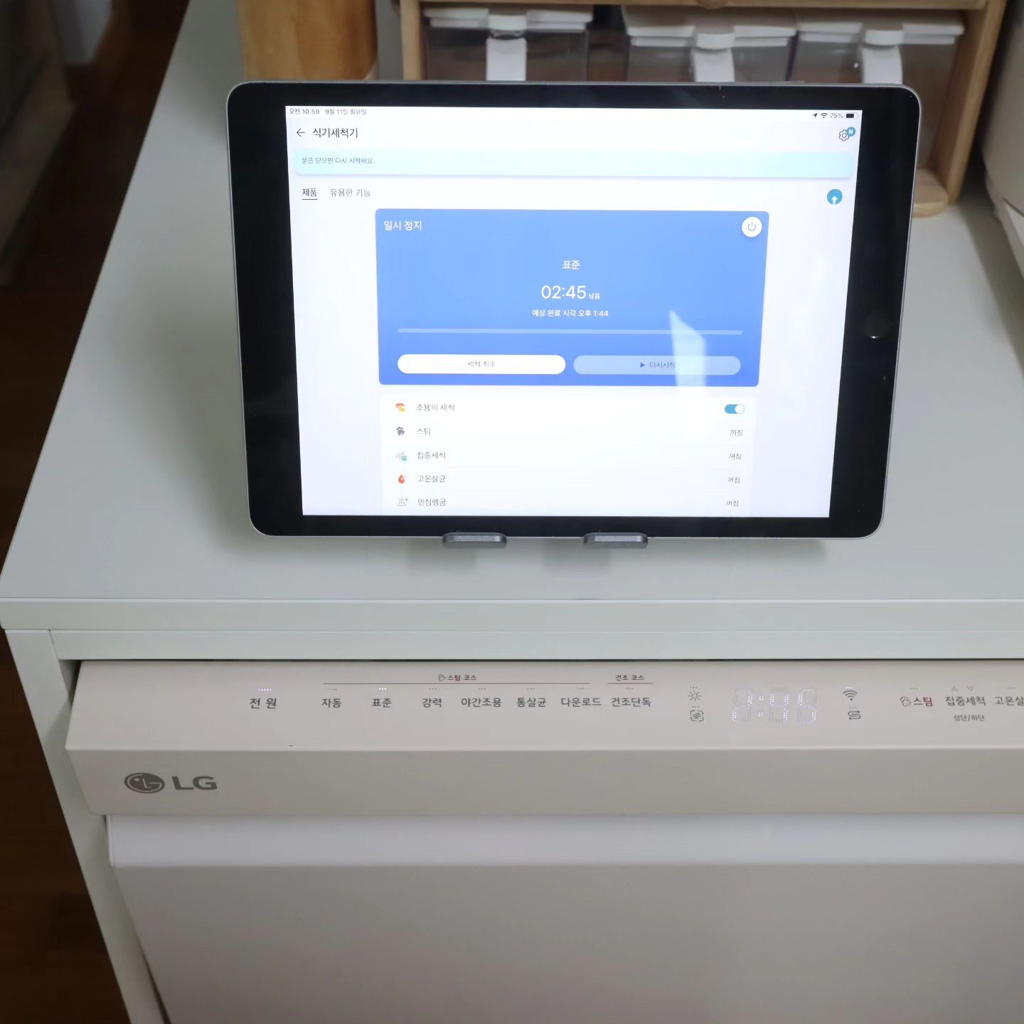 LG 식기세척기 위에 놓인 태블릿, 식기세척기 앱에서 세척 상태와 타이머가 표시된 화면