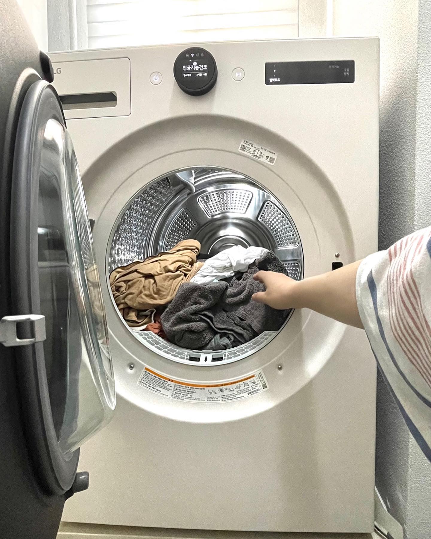 LG 트롬 오브제컬렉션 건조기 문을 열고 의류를 꺼내려고 하는 모습.