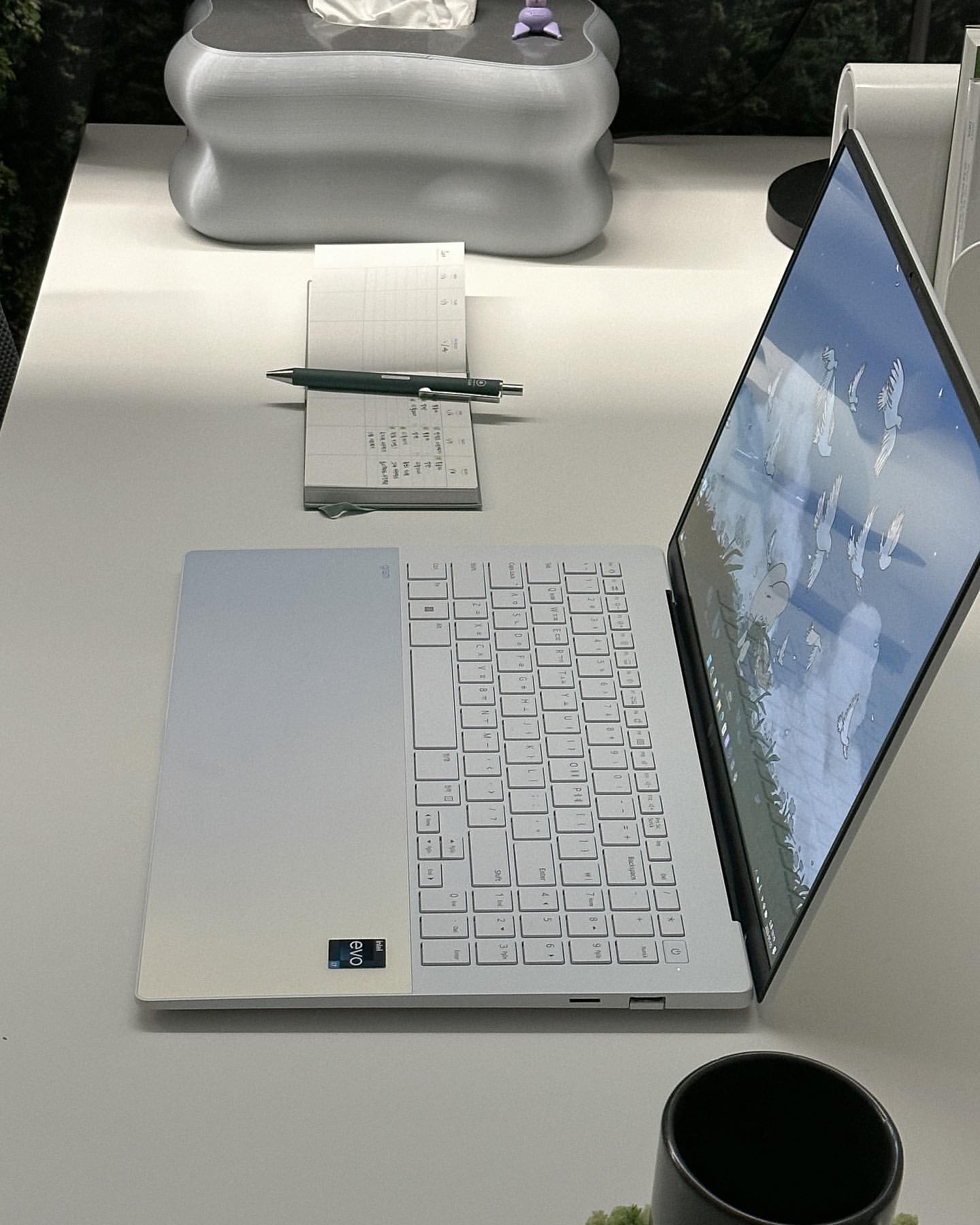 흰색 책상 위에 열려 있는 LG 그램 Style 노트북과 펜, 노트가 놓여 있는 모습.