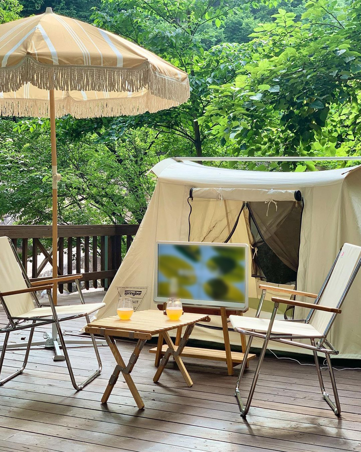 우산 아래 야외 공간에서 LG 룸앤 TV가 텐트 앞에 설치되어 자연 화면이 표시된 모습.