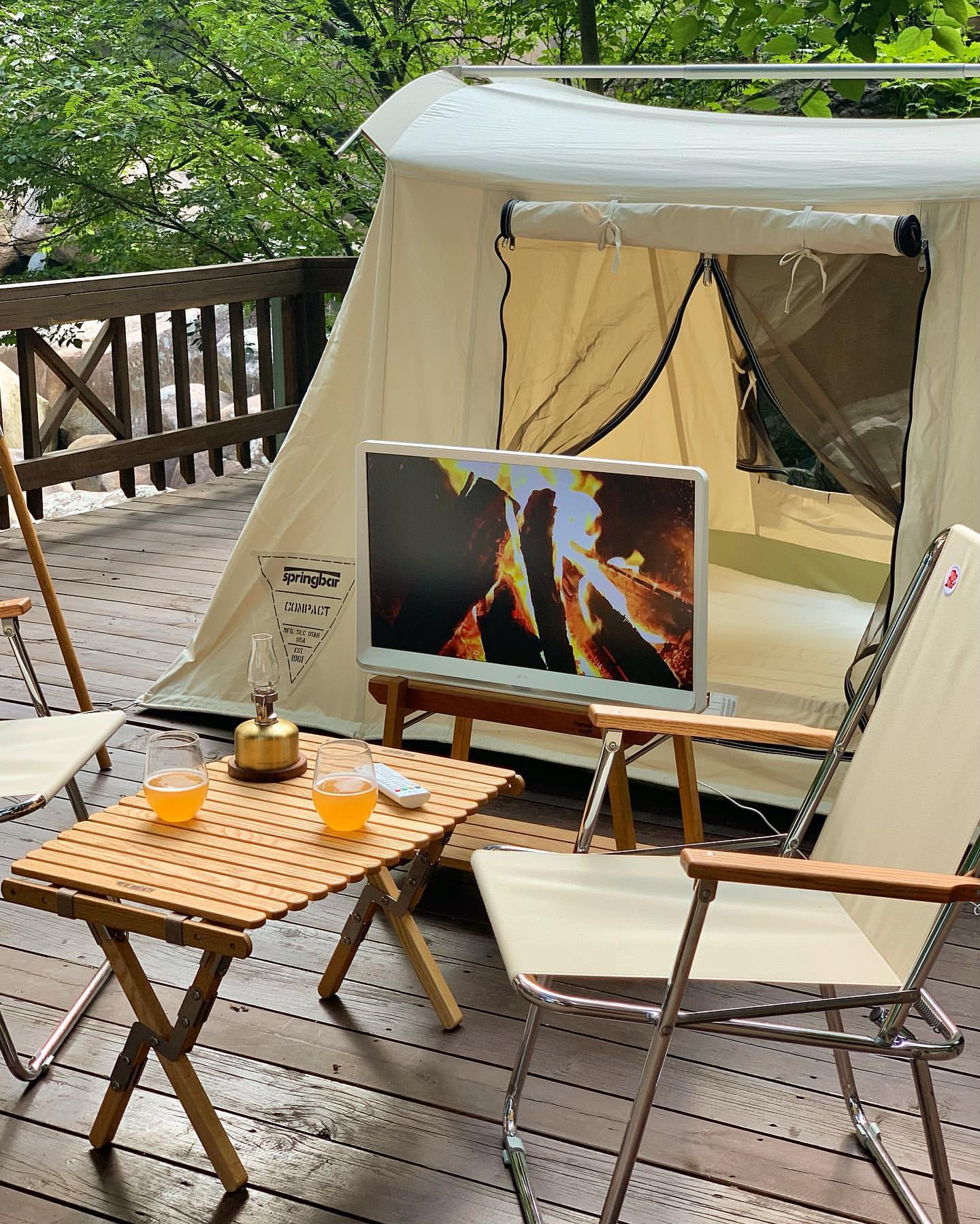흰색 텐트 앞에 설치된 테이블 위 LG 룸앤 TV에서 모닥불 화면이 표시된 모습.