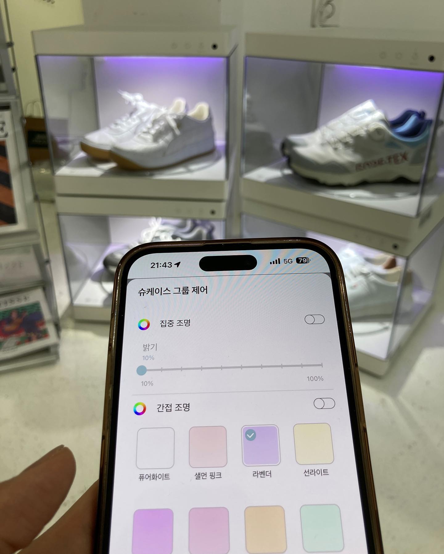 스마트폰 화면에 슈케이스 조명을 제어하는 인터페이스가 표시되고, 뒤로 흰색 슈케이스들이 보입니다.
