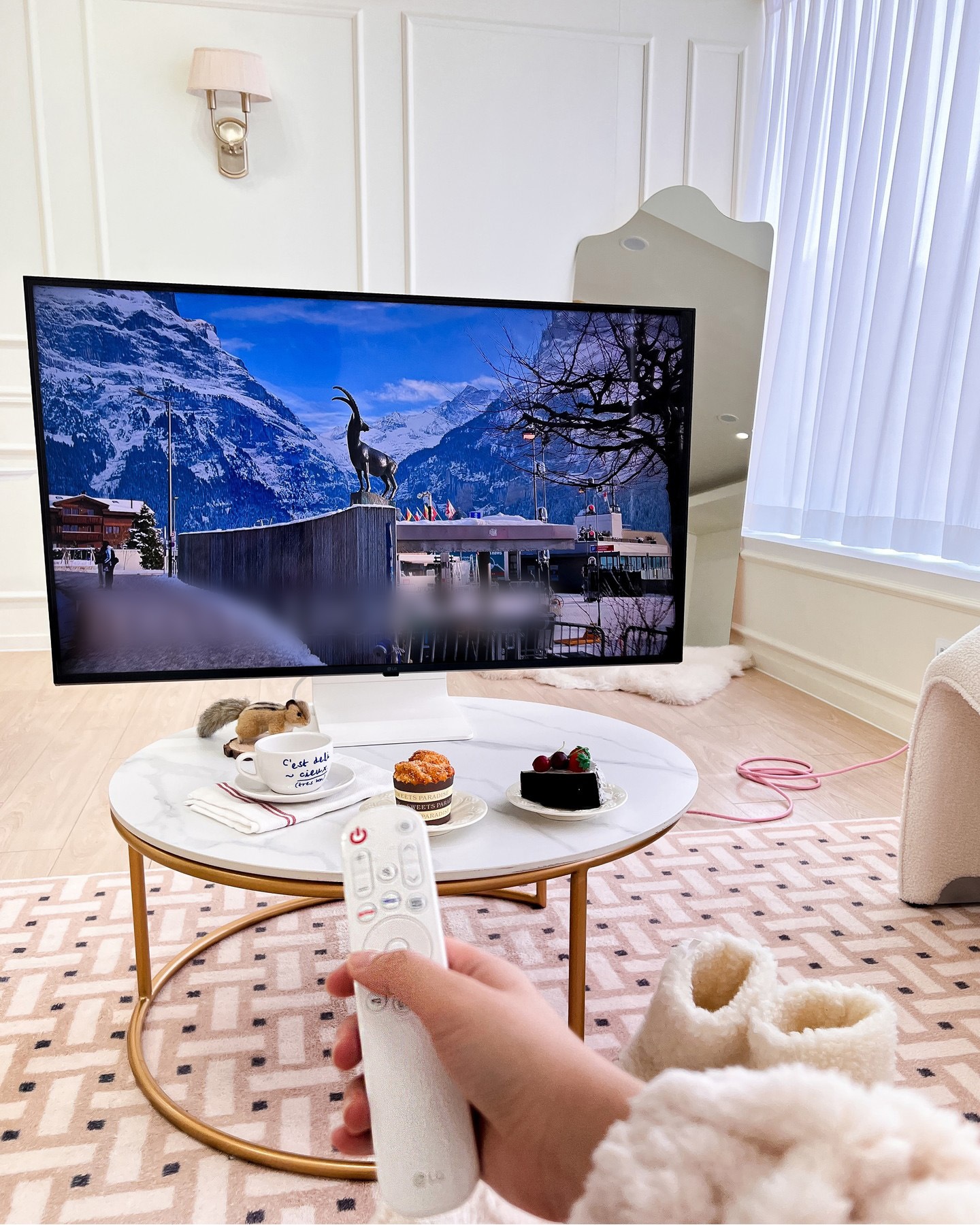 대리석 테이블 위 디저트를 앞에 두고 TV 화면에 산과 도시 풍경이 보이는 모습.