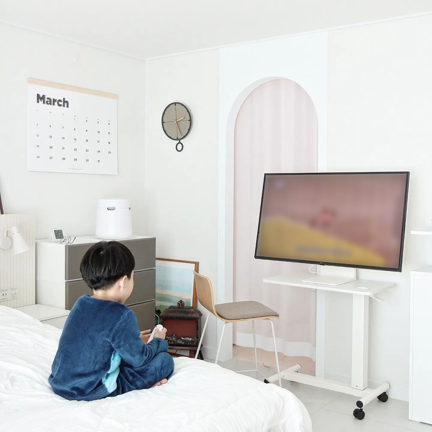 LG 스마트 모니터 앞 침대에 아이가 앉아서 리모컨을 누르고 있는 모습.