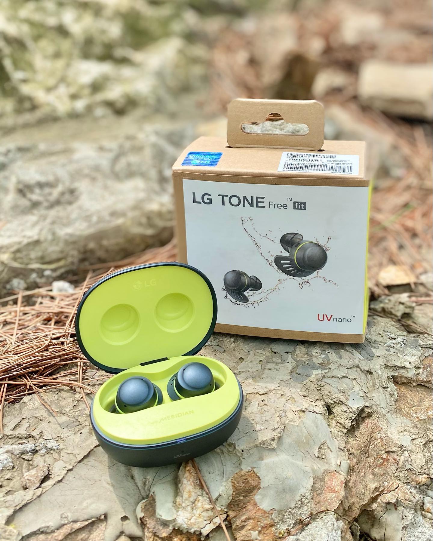 돌 위에 놓인 블랙과 옐로우 컬러의 LG TONE Free Fit 무선 이어폰과 패키지 상자