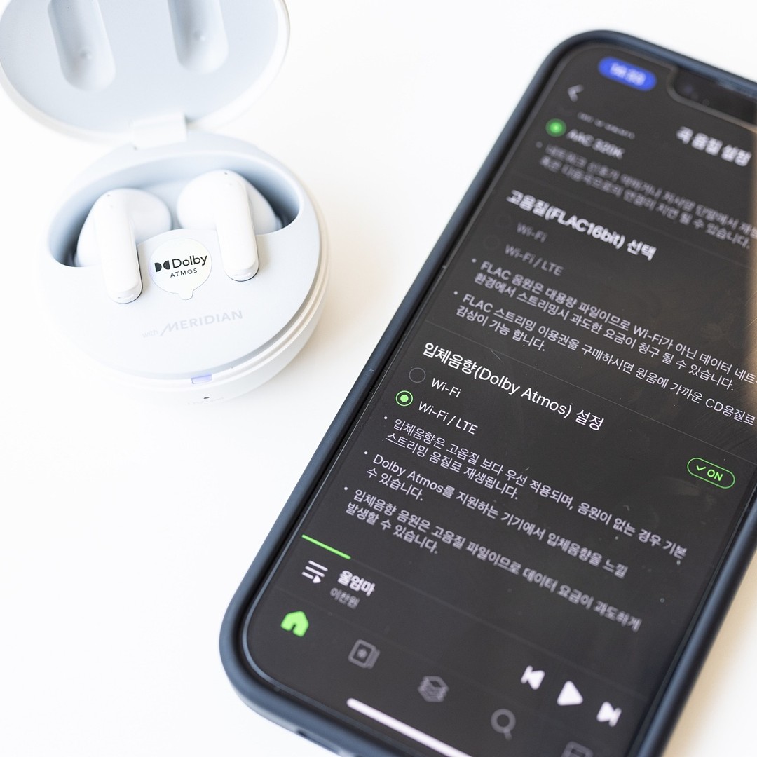 LG흰색 LG 톤프리 이어폰 충전 케이스와 Dolby Atmos 설정이 나타난 스마트폰 화면