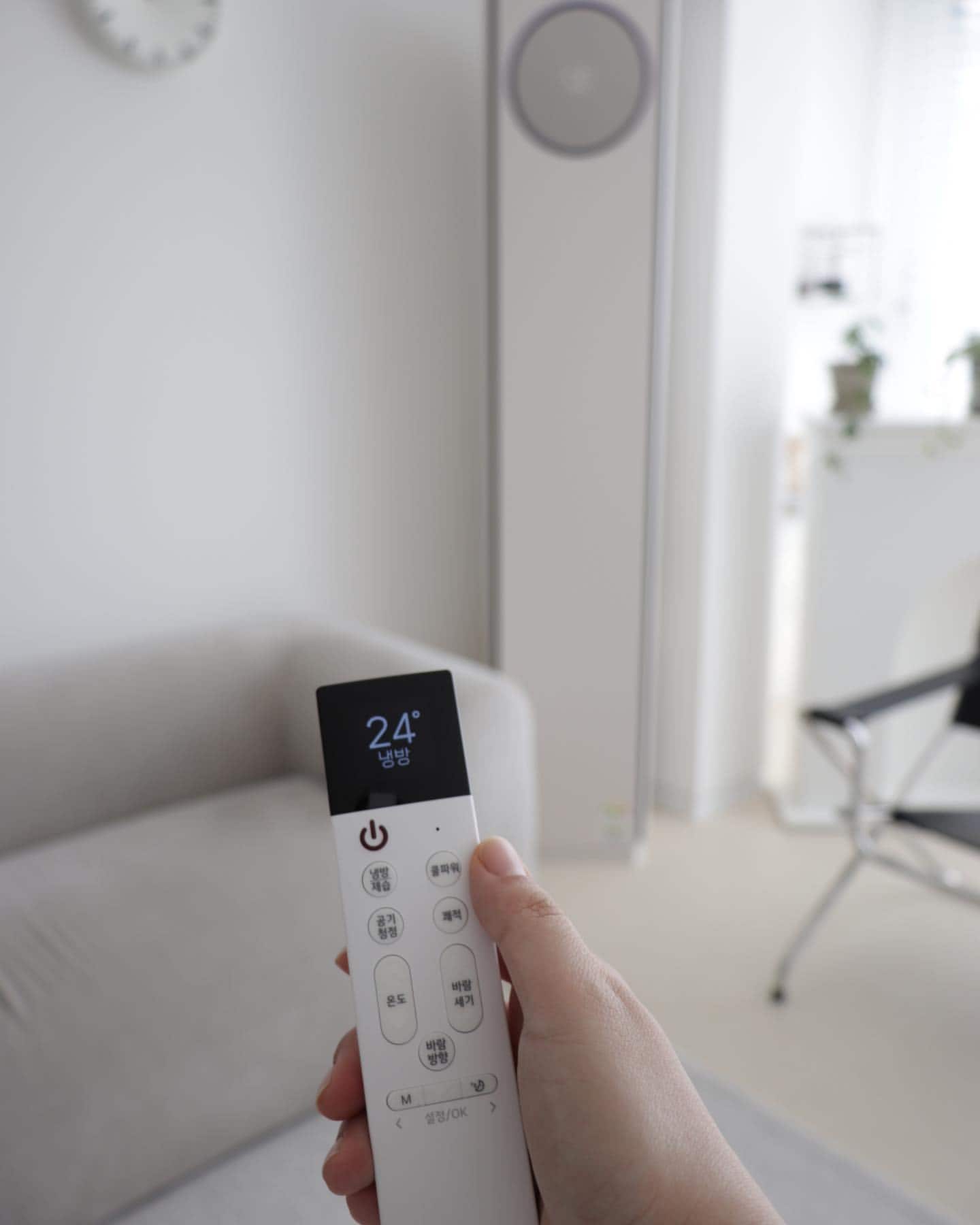 LG 휘센 오브제컬렉션 타워에어컨 리모컨 화면에 냉방 24도가 표시된 모습과 함께 실내 거실이 배경으로 보이는 모습.