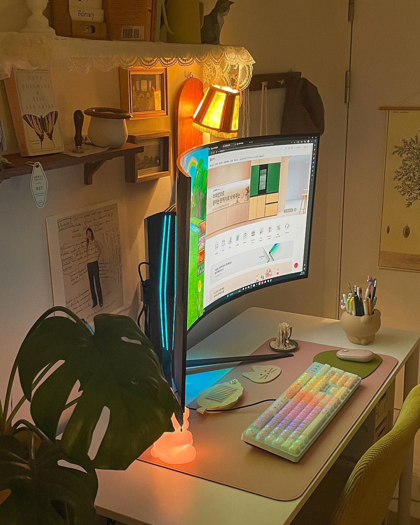 책상 위에 LG 울트라와이드 게이밍 모니터가 측면에서 보이고, RGB 조명이 켜진 키보드와 깔끔하게 정리된 필기 도구가 놓인 모습.