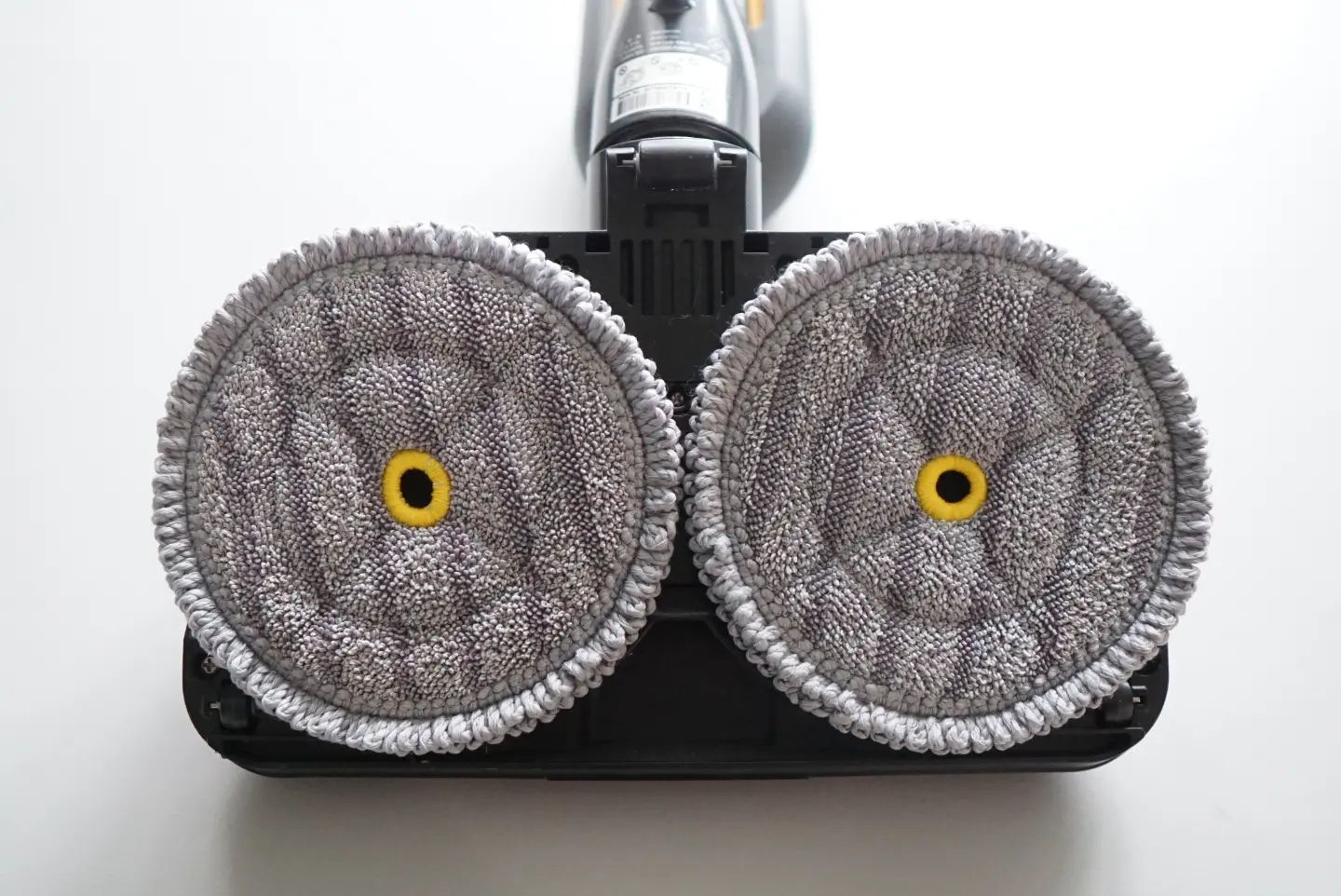 무선 청소기의 하단 부분으로, 두 개의 회전형 극세사 걸레 패드가 부착된 모습. 패드는 회색이며 중앙에 노란색 고정 링이 있음