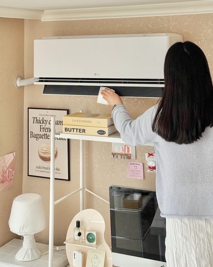 방 안에서 에어컨을 손질하는 사용자. 잘 정돈된 책상과 조명등, 포스터, 소품들이 따뜻하고 아늑한 분위기를 만들어냄.