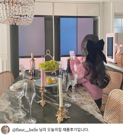 LG 디오스 오브제컬렉션 무드업 냉장고가 배경에 보이는 장면으로, 한 여성이 스마트폰을 들고 냉장고 앞에서 서 있습니다. 테이블 위에는 와인, 과일, 촛대가 놓여 있으며, 하단에는 '@fleur__belle 님의 오늘의집 제품후기입니다.'라는 텍스트가 포함되어 있습니다.