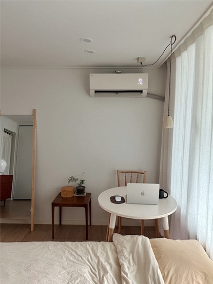 침실에 설치된 LG 휘센 사계절에어컨이 보이며, 침대와 작은 책상, 의자가 배치되어 있습니다. 공간은 따뜻하고 아늑한 분위기를 자아냅니다.