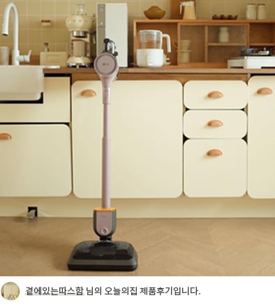 우드톤 주방에 세워진 LG 코드제로 오브제컬렉션 A9S 무선 청소기의 모습. 하단에 '곁에있는따스함 님의 오늘의집 제품후기입니다.'라는 텍스트가 포함되어 있음.