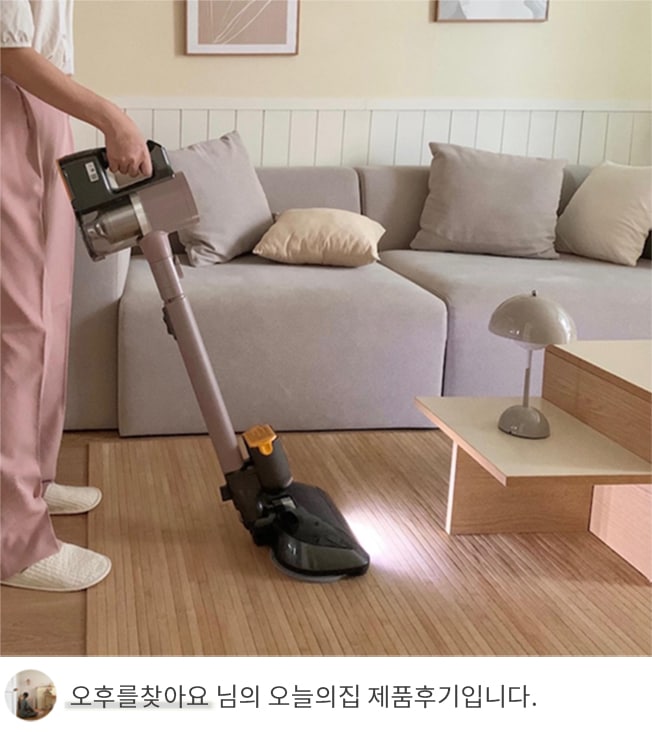 LG 코드제로 오브제컬렉션 A9S 무선청소기를 사용해 거실 바닥을 청소하는 모습. 사용자가 청소기의 손잡이를 잡고 있으며, 청소기에서 나오는 조명이 바닥을 밝히고 있음. 뒤에는 베이지 톤의 소파와 라운드 테이블이 배치되어 따뜻하고 아늑한 거실 분위기를 보여줌. 하단에는 '오후를찾아요 님의 오늘의집 제품후기입니다.'라는 텍스트가 포함되어 있음.