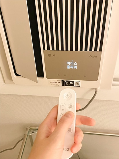 LG 휘센 오브제컬렉션 엣지를 리모컨으로 조작하는 모습. 사용자의 손이 리모컨을 잡고 있으며, 디스플레이에 '아이스 쿨파워'라는 모드가 표시되어 있어 강력한 냉방 기능을 강조함.