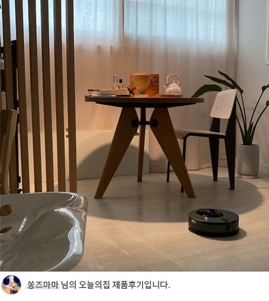 LG 코드제로 오브제컬렉션 M9 로봇청소기가 나무 식탁과 의자 옆에서 작동 중인 모습. 식탁 위에는 주전자와 컵이 놓여 있어 따뜻한 분위기를 연출하며, 하단에는 '쏭즈마마 님의 오늘의집 제품후기입니다.'라는 텍스트가 포함되어 있어 사용자의 제품 경험을 나타냅니다.