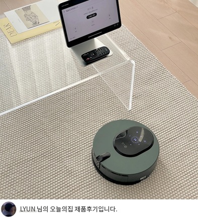 투명한 테이블 아래에서 LG 코드제로 오브제컬렉션 M9 로봇청소기가 청소를 하고 있으며, 테이블 위에는 태블릿과 리모컨이 놓여 있습니다. 하단에는 'LYUN 님의 오늘의집 제품후기입니다.'라는 텍스트가 포함되어 있음.