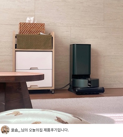LG 코드제로 오브제컬렉션 R9 로봇청소기가 충전 거치대에 연결된 모습. 충전 거치대는 어두운 그린 컬러로 세련된 디자인을 갖추고 있으며, 옆에는 소품과 수납장이 배치되어 있습니다. 하단에는 '윤솜_ 님의 오늘의집 제품후기입니다.'라는 텍스트가 포함되어 사용자의 후기를 강조합니다.