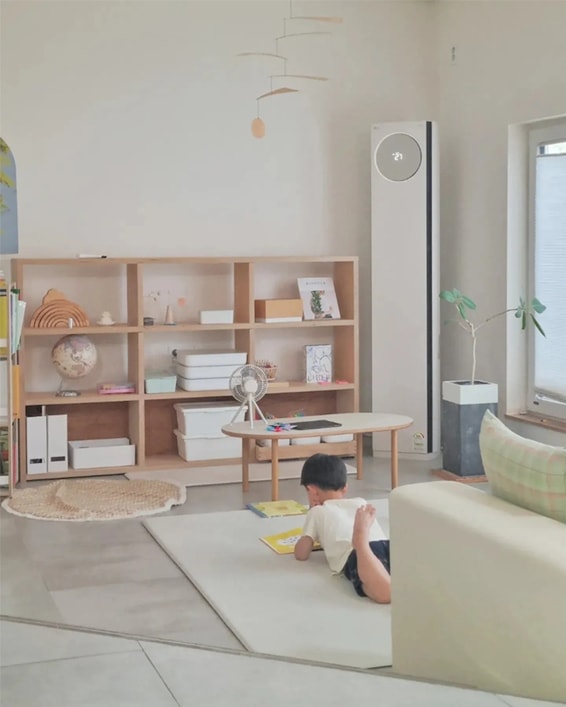 LG 휘센 오브제컬렉션 타워 에어컨이 거실에 배치되어 있고 어린아이가 바닥에 엎드려 책을 읽는 모습. 책장이 놓인 아늑한 거실에서 타워 에어컨이 세련되고 모던한 인테리어와 조화를 이루며, 자연스러운 공간 연출을 보여줍니다.