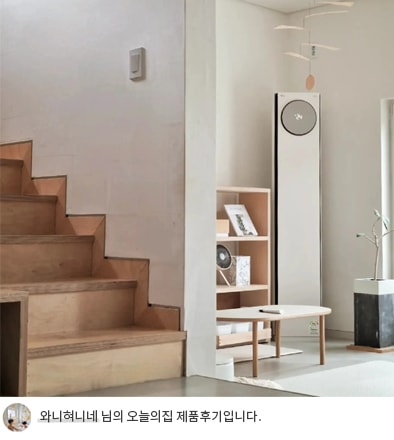 LG 휘센 오브제컬렉션 타워 에어컨이 계단 옆에 배치된 모습. 에어컨 주변은 간결한 인테리어 소품으로 꾸며져 있으며, 공간을 차지하지 않는 슬림한 디자인이 강조됩니다. 하단에는 '와니혀니네 님의 오늘의집 제품후기입니다.'라는 텍스트가 포함되어 있어 사용자의 제품 후기를 나타냅니다.