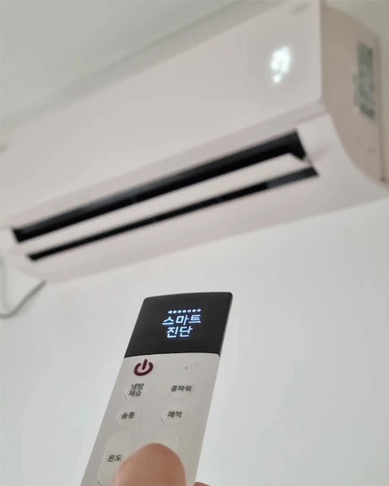 LG 휘센 오브제컬렉션 벽걸이 에어컨을 리모컨으로 조작하는 모습. 에어컨의 작동 상태가 디스플레이에 표시되어 있으며, 사용자가 간편하게 조작할 수 있는 직관적인 인터페이스를 보여줍니다.