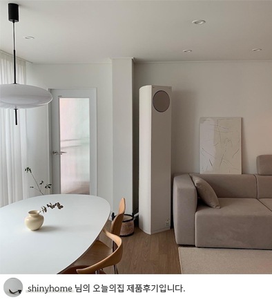 LG 휘센 오브제컬렉션 타워에어컨이 다이닝룸 옆 벽에 설치된 모습. 옆에는 화이트 톤의 타원형 식탁과 나무 소재 의자가 배치되어 있으며, 벽에는 미니멀한 그림과 도어가 설치되어 있어 심플한 인테리어가 강조됨. 하단에는 'shinyhome 님의 오늘의집 제품후기입니다.'라는 텍스트가 포함되어 있음.