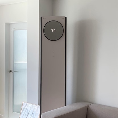 LG 휘센 오브제컬렉션 타워에어컨이 거실 구석에 설치된 모습. 베이지톤의 소파와 주변 인테리어와 잘 어우러지며, 타워형 에어컨의 직관적인 디스플레이와 라운드형 무드 조명이 돋보이는 디자인.