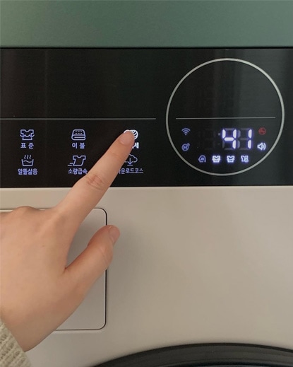 LG 트롬 오브제컬렉션 워시타워 컴팩트의 조작 패널을 손가락으로 누르고 있는 모습. 다양한 세탁 옵션과 직관적인 조작 패널이 강조되어 사용자의 편리함을 보여줍니다.